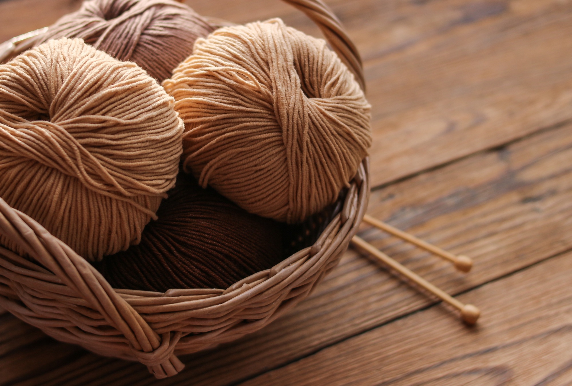 Knitting needles and yarn in a wicker basket on a wooden background. Handicraft day
